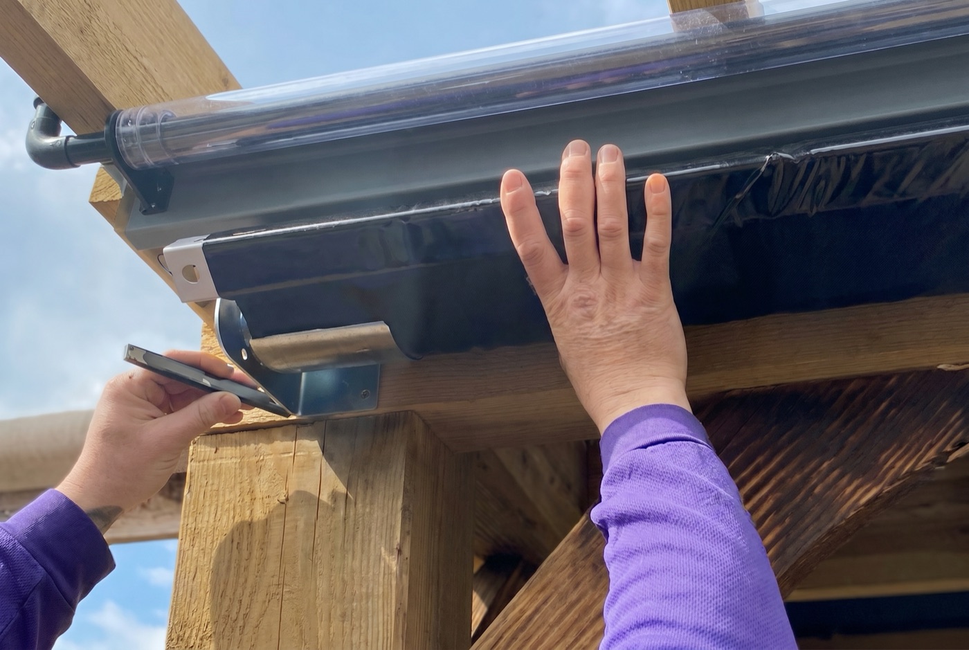 Marking the bracket position on a timber pergola beam below the clear PVC roller blind cassette