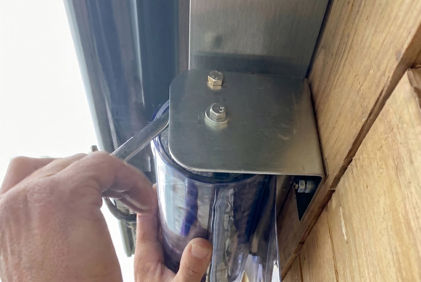 Removing the locking-off bolt from the metal end bracket to release the blind's spring mechanism