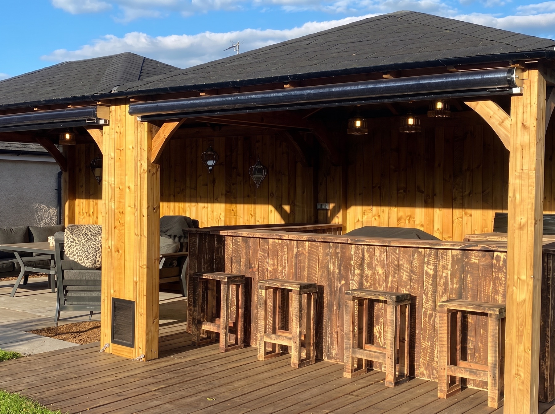 Timber garden bar with roller blinds rolled up under the roof line, ready for service