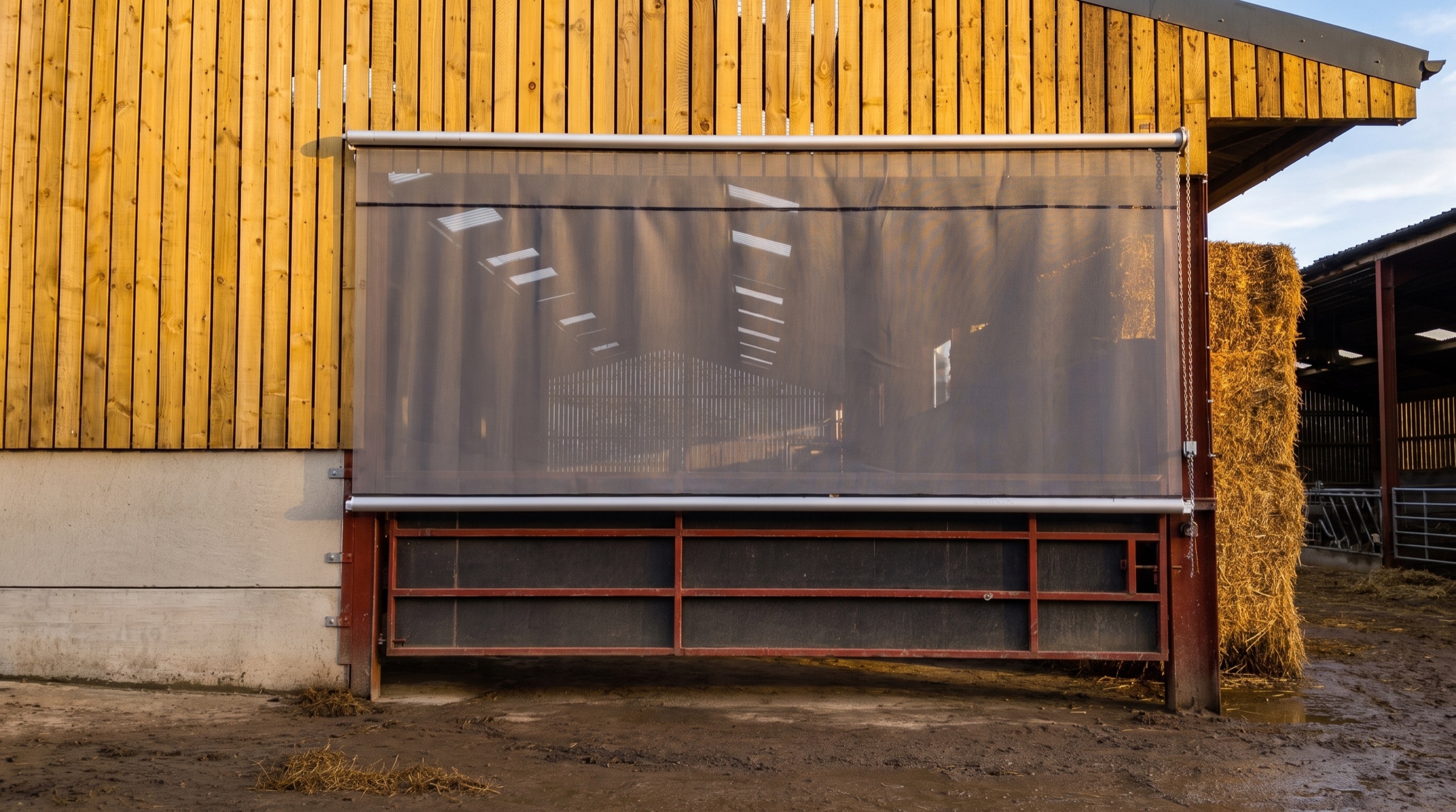 Mesh roller blind across a timber clad barn opening on a working farm
