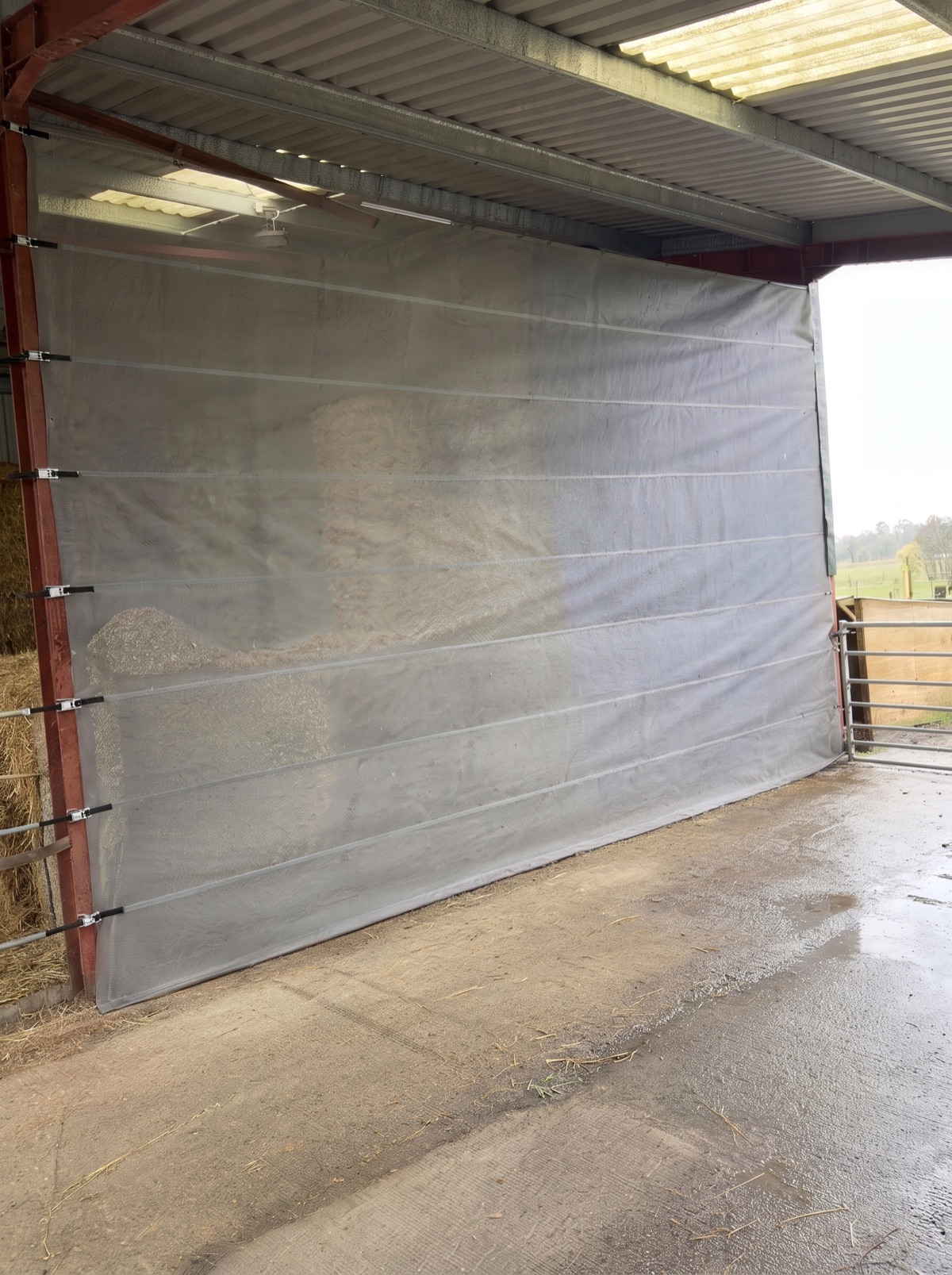 Windbreak screen protecting stored straw inside a barn bay